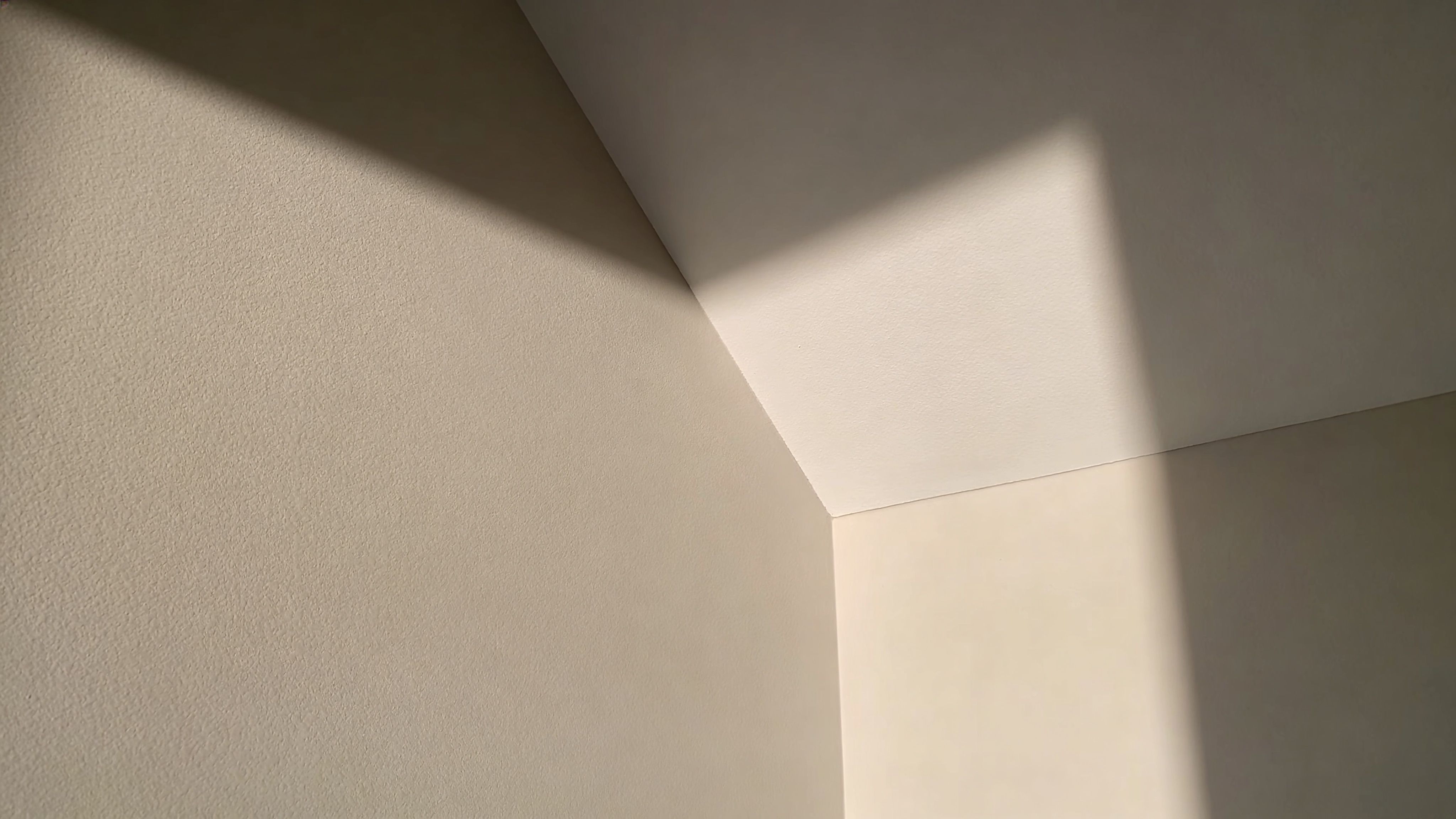 A corner view showing sunlight casting sharp shadows across a ceiling and two adjacent textured walls.