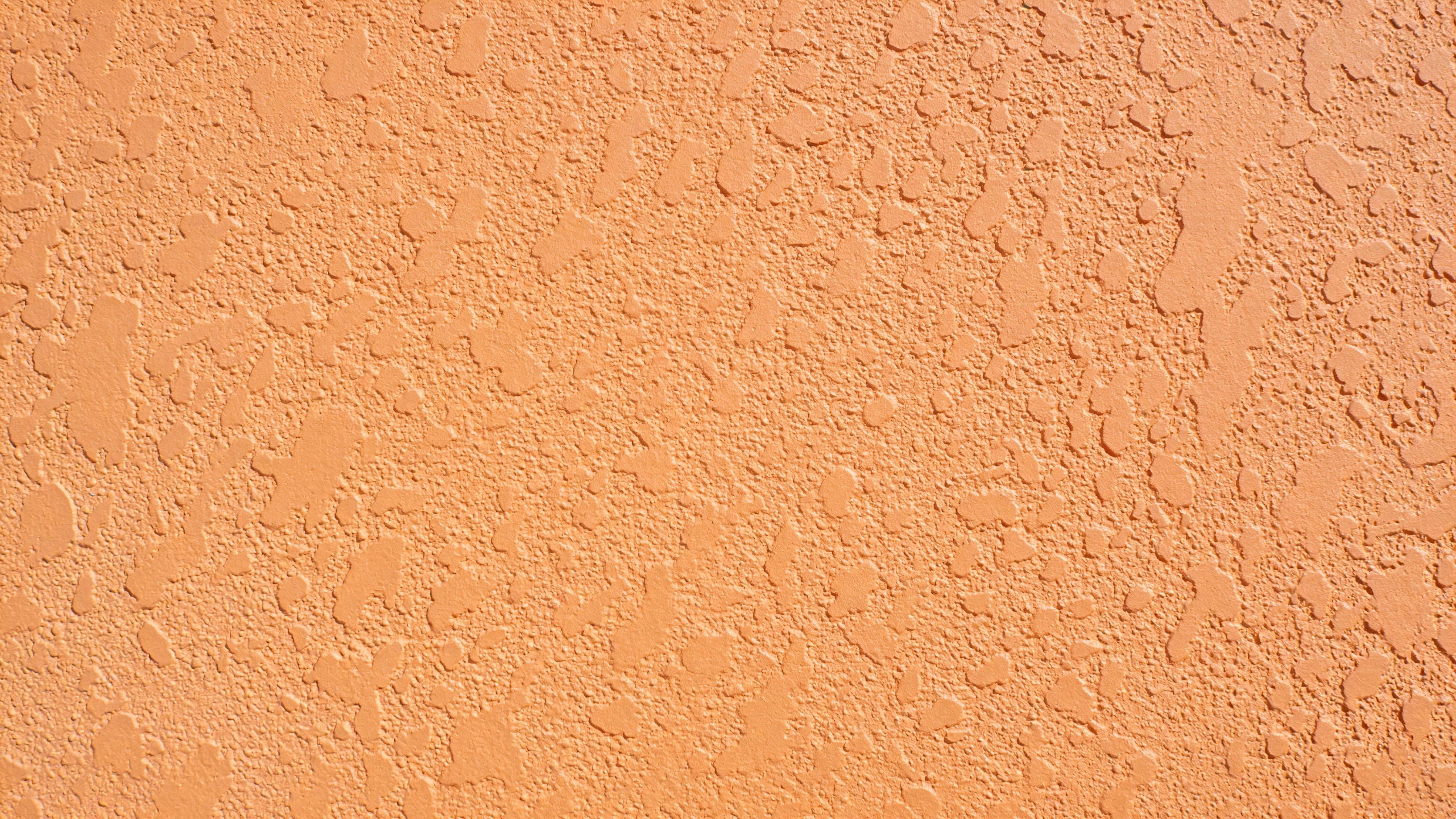 A close-up view of a light orange colored wall with a rough, textured stucco surface finish.