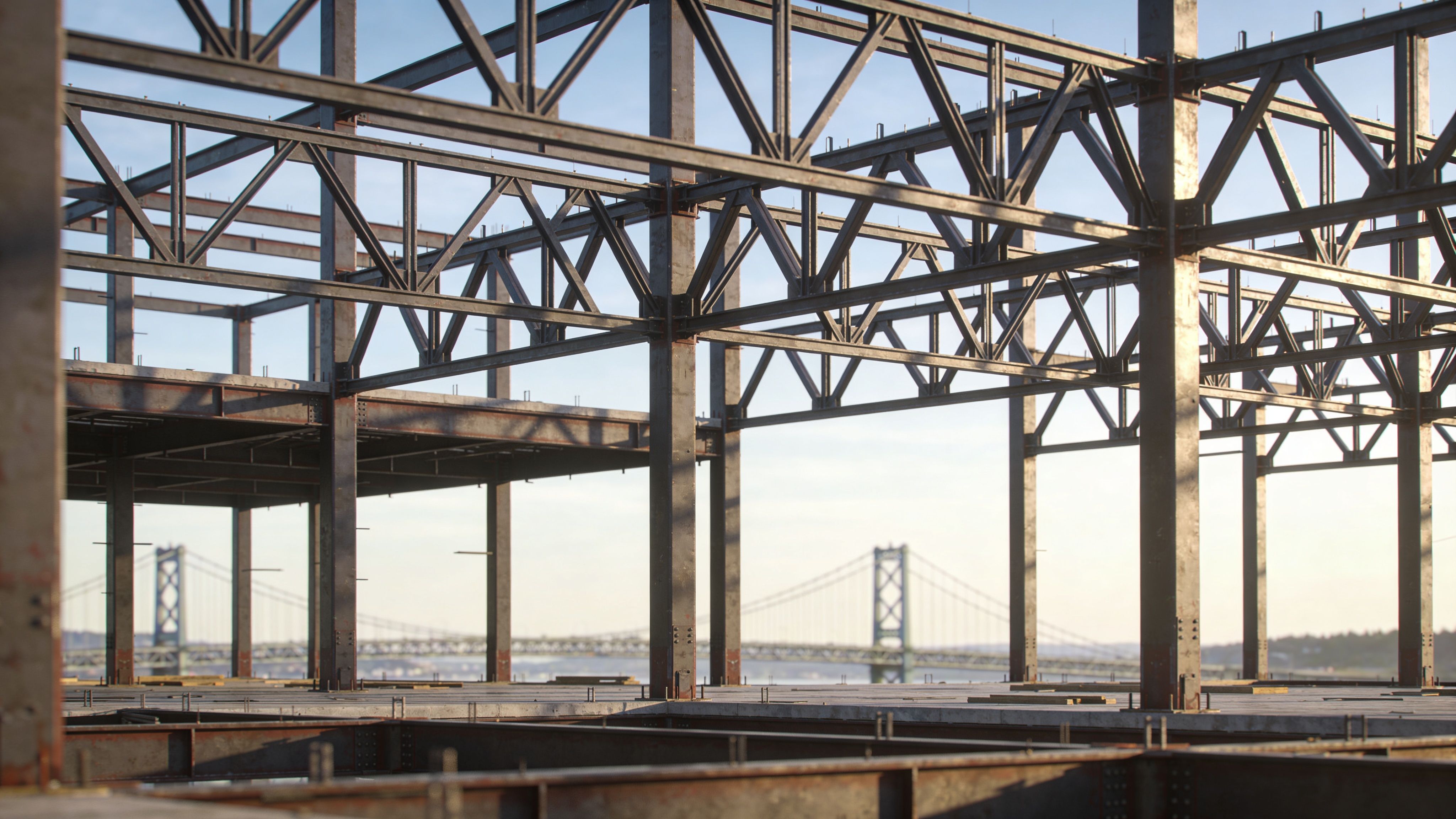 A steel frame structure of a building under construction overlooking a suspension bridge in the distance.