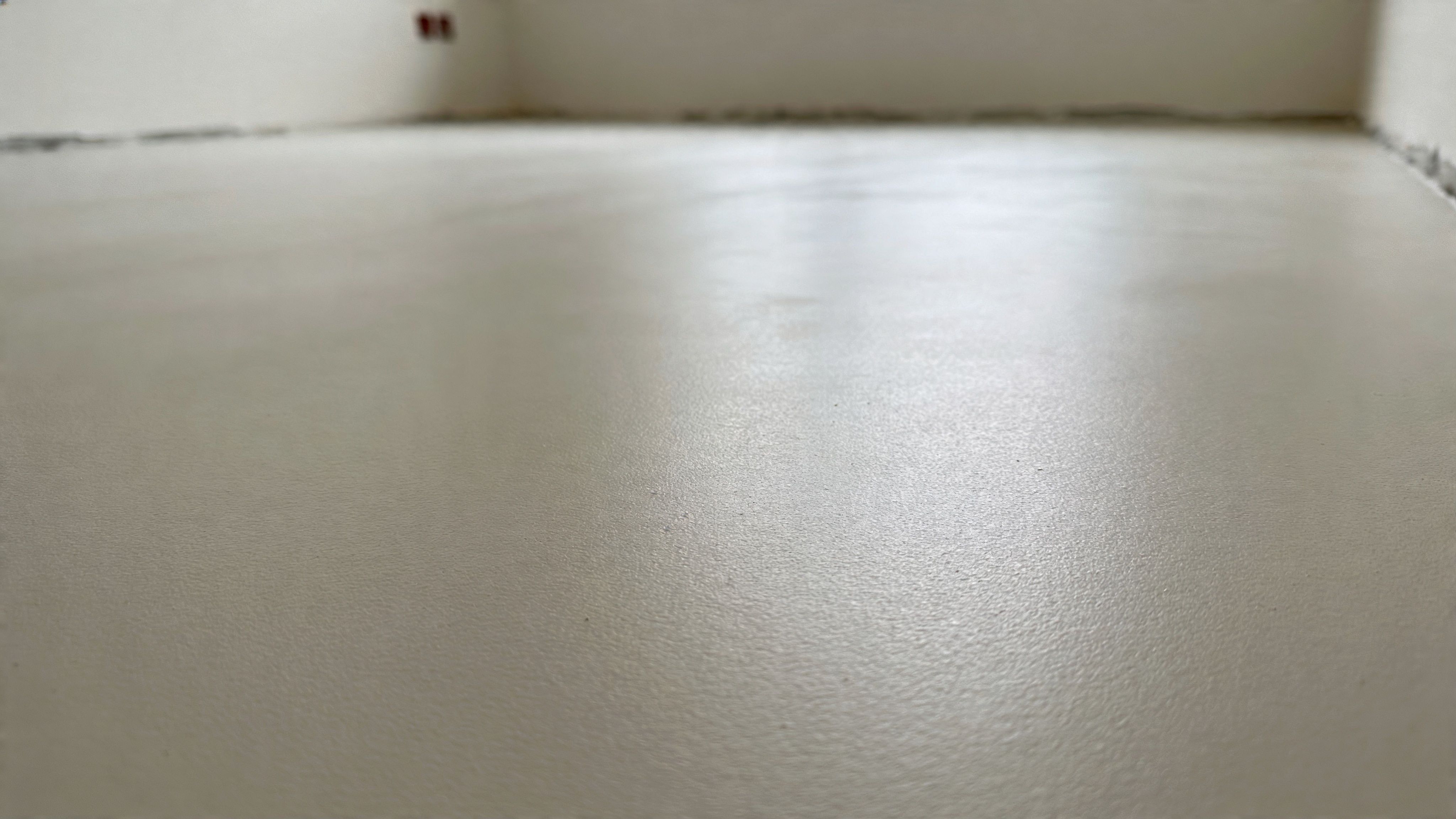 A smooth, freshly applied leveled floor surface inside a room under construction with white walls.