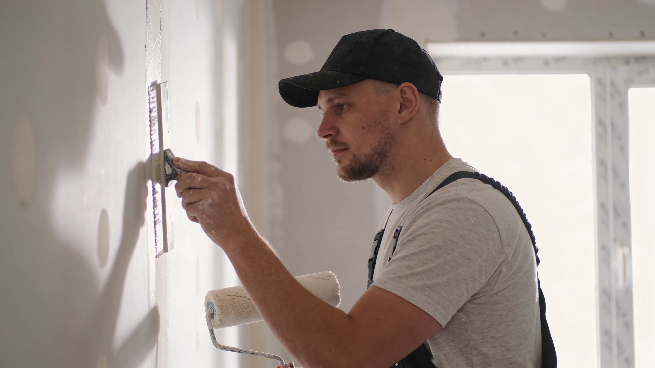 A professional construction worker skillfully applying joint compound to a drywall seam with a putty knife.