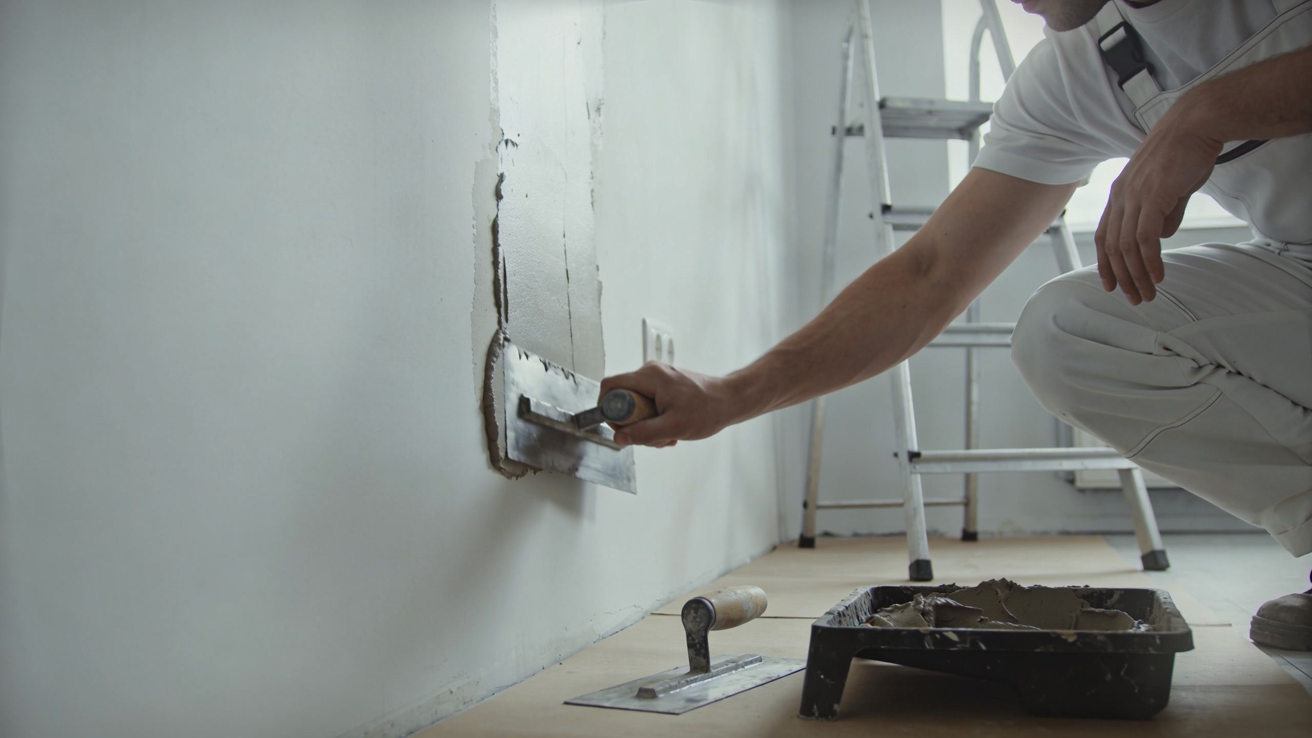 A professional construction worker applying plaster to a wall with a metal trowel in a renovated room.