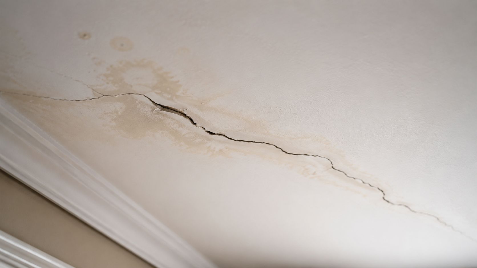A close up view of a damaged ceiling with significant water stains and a large structural crack.
