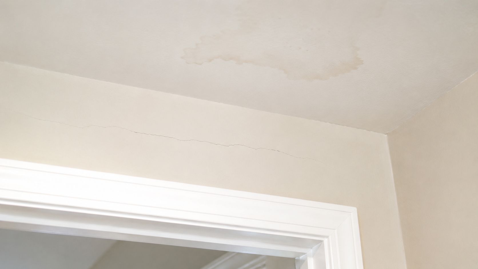 A crack above a door frame and a water stain on the drywall ceiling, showing damage.