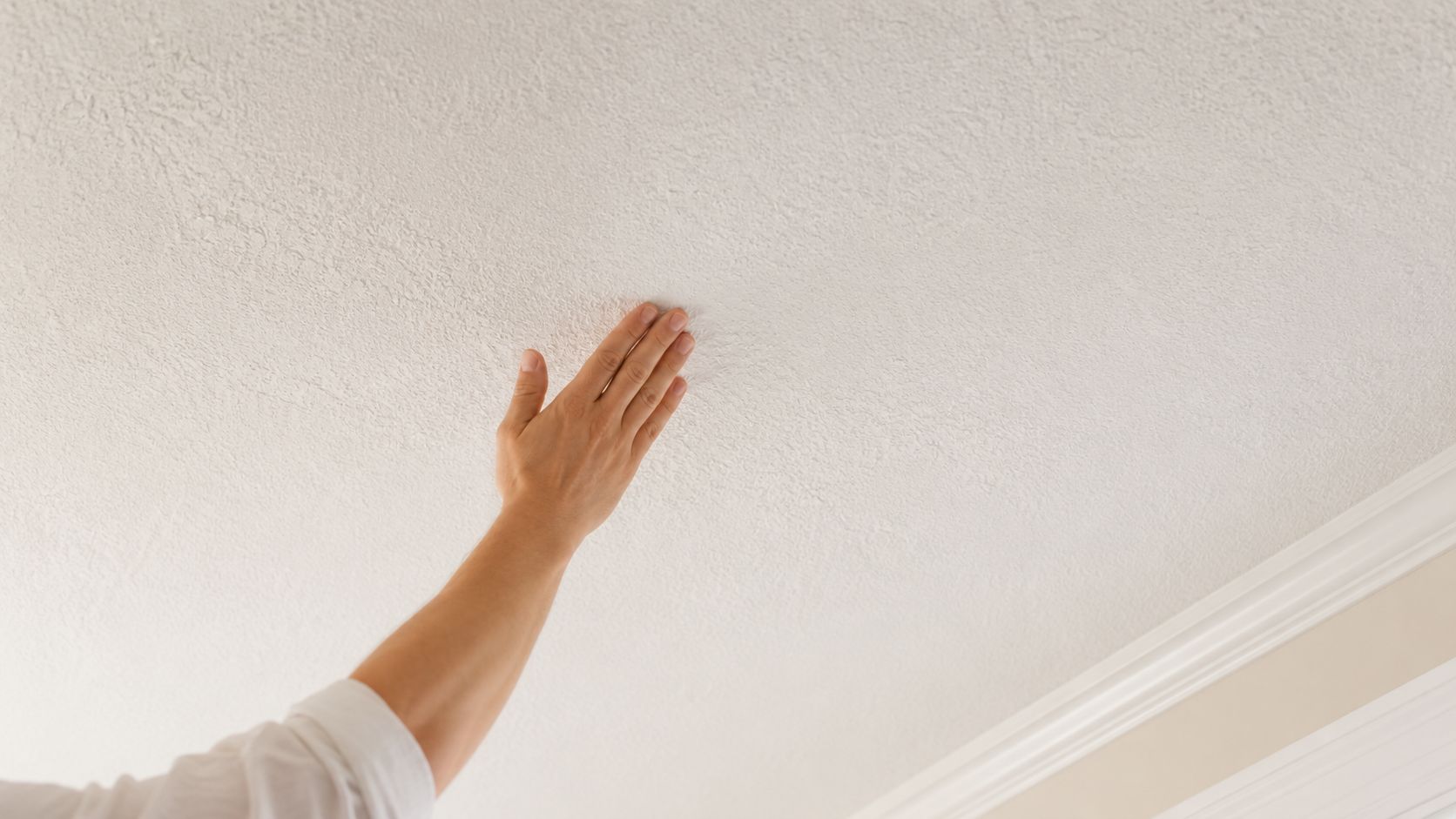 A person touching a textured white ceiling with their hand to inspect the surface finish