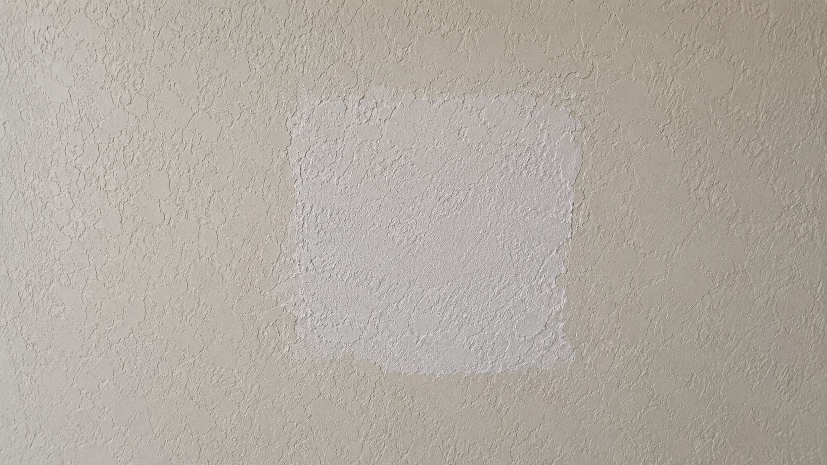 A square section of wall with a fresh white patch of drywall knockdown texture applied.